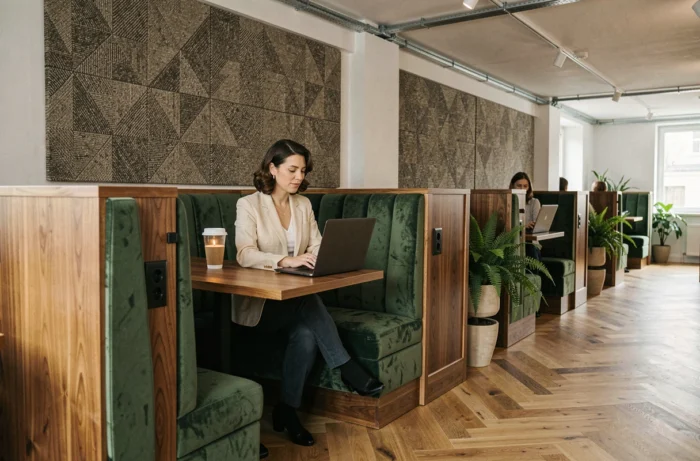 Femme travaillant dans un espace de coworking avec banquettes sur mesure en velours vert et séparateurs en noyer intégrés